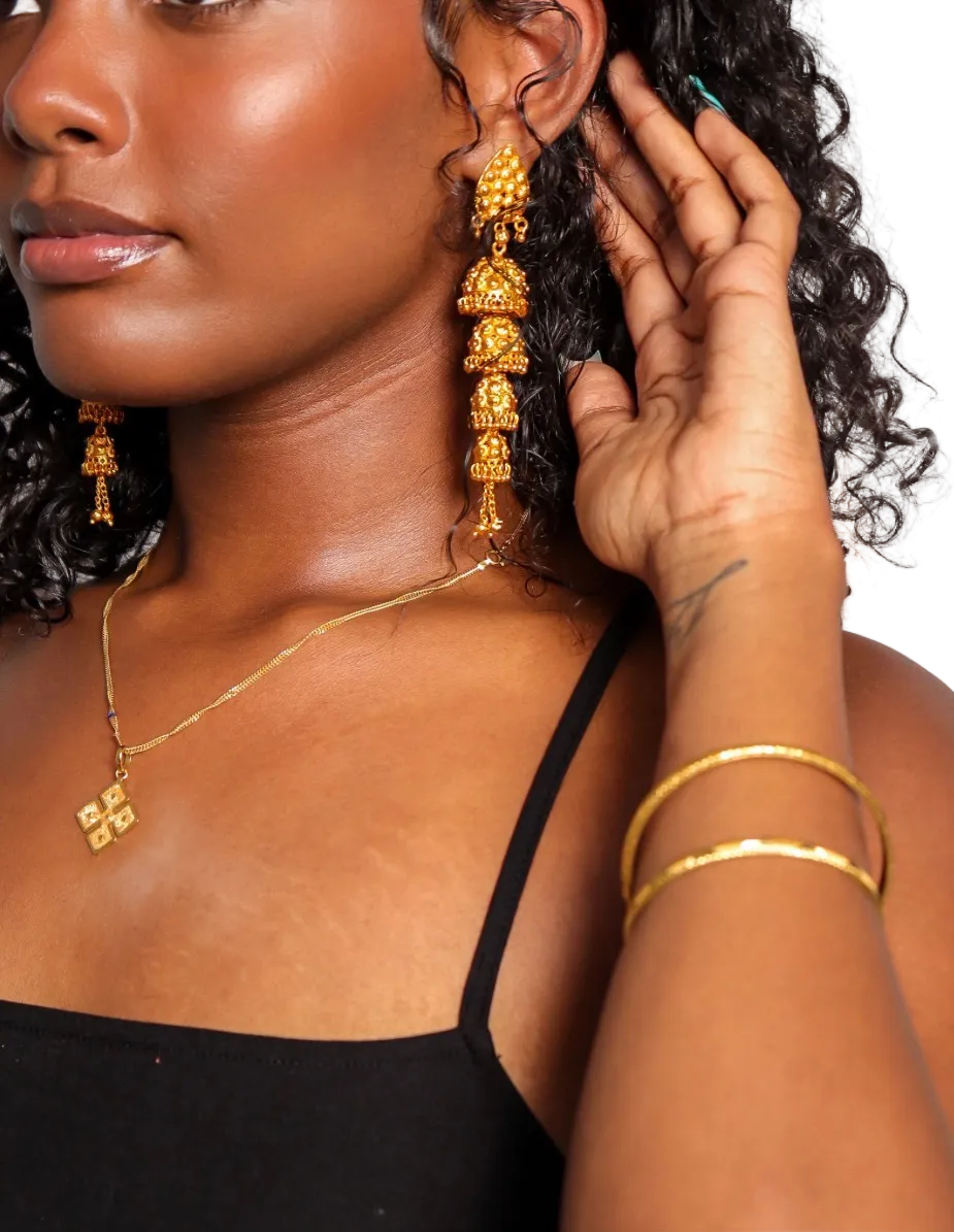 Woman wearing gold earrings and a necklace, with one hand adjusting the earring.